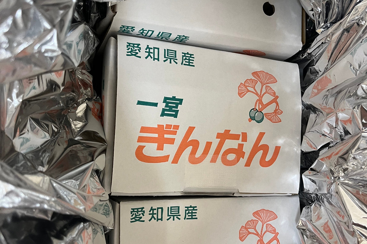 Three stacked white paper packages of Japanese ginkgo biloba leaves, branded with orange and green text, nestled inside crumpled silver foil packaging.